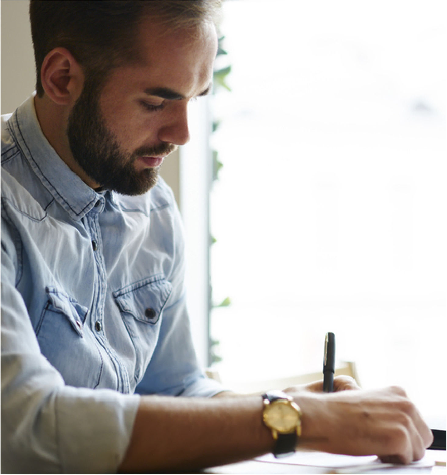 Man sat at a desk making notes on a document he is reviewing.
